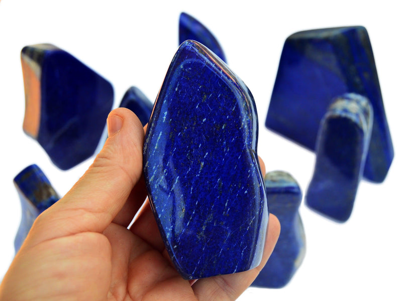 Lapis lazuli free form chunky crystal 80mm on hand with background with some crystals on white