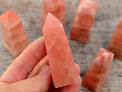 One rose calcite obelisk crystal 65mm on hand with background with some crystals on wood table