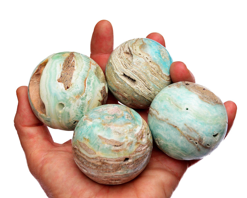 Four blue aragonite crystal spheres 55mm-65mm on hand with white background