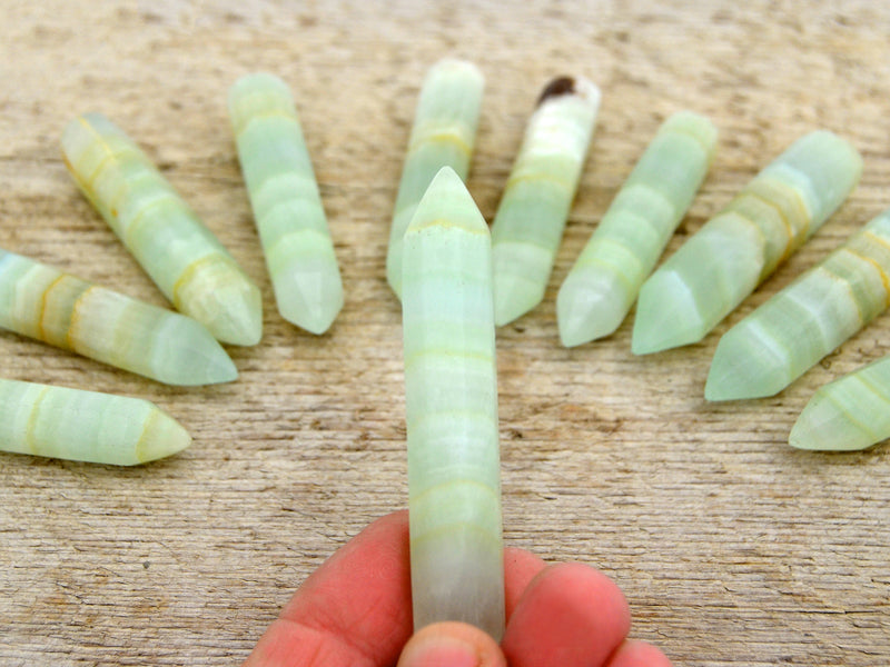 One green pistachio calcite faceted point 65mm on hand with background with some points