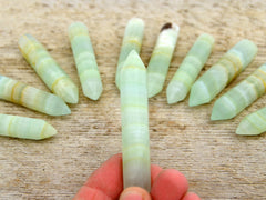 One green pistachio calcite faceted point 65mm on hand with background with some points
