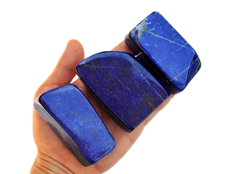 Three lapis lazuli free form crystals 55mm-80mm on hand with white background