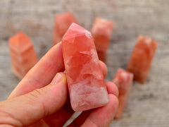 One rose calcite obelisk crystal 60mm on hand with background with some crystals on wood table