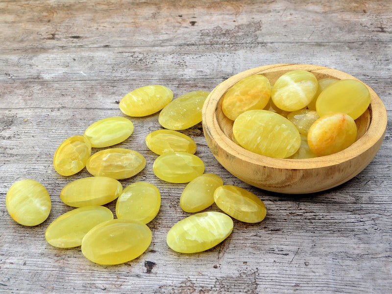 Some lemon calcite palm stones inside a wood bowl with background with some stones on wood table