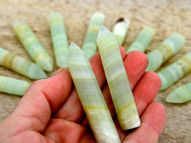 Two pistachio calcite faceted points 70mm on hand with background with some points