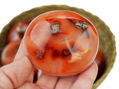 One red carnelian crystal palm stone 60mm on hand with background with some specimens inside a basket on white