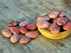 Several rose calcite palm stones 50mm-75mm inside a bowl with background with some crystals on wood table