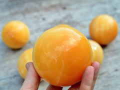 One large orange calcite 75mm on hand with background with some balls 