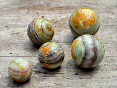 Five pink banded onyx spheres 60mm-95mm on wood table