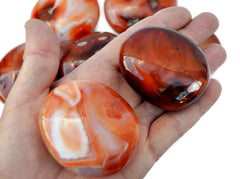 Two carnelian palm stones 40mm-50mm on had with background with some stones on white