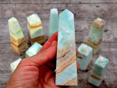 One caribbean blue calcite crystal tower 100mm on hand with wood background