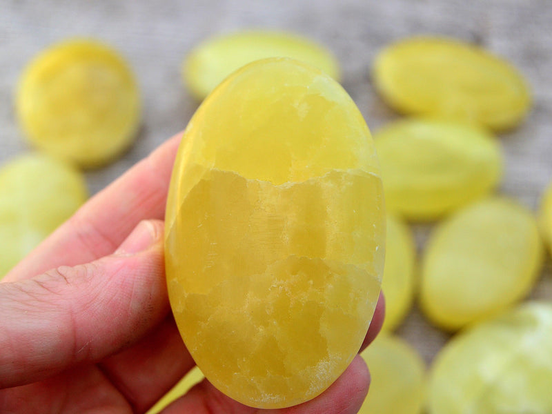 One lemon yellow calcite palm stone 60mm on hand with background with some crystals on wood table