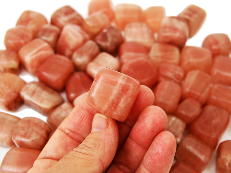 One rose calcite tumbled 20mm on hand with background with several stones on white