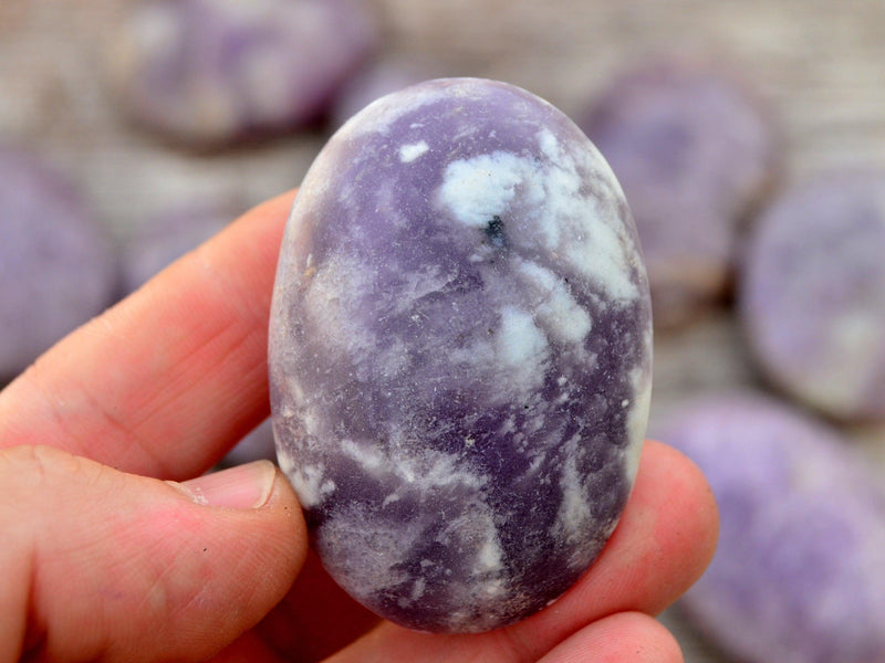 Lepidolite palm stone 70mm on hand with background with several crystals on wood table