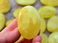One lemon yellow calcite palm stone 55mm on hand with background with some crystals on wood table