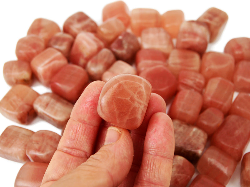 One rose calcite tumbled 30mm on hand with background with several stones on white