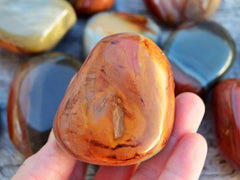 One big polychrome jasper tumbled crystal on hand with background with some stones on wood table