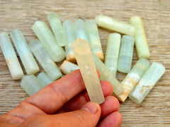 One small caribbean calcite faceted crystal point 60mm on hand with background with several crystals on wood table