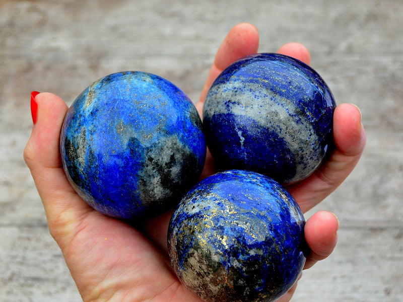 Three blue lapis lazuli sphere crystals 60mm on hand with wood background