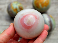 One pink banded onyx sphere 60mm on hand with background with some stones on wood table