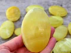 One lemon yellow calcite palm stone 80mm on hand with background with some crystals on wood table