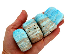 Four small blue aragonite free form stones 50mm on hand with white background