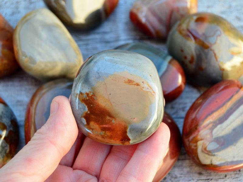 One large polychrome jasper tumbled crystal on hand with background with some stones on wood table