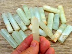 One small caribbean calcite faceted crystal point 55mm on hand with background with several crystals on wood table
