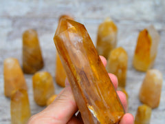 One large yellow hematoid quartz tower on hand with background with some crystal points on wood table