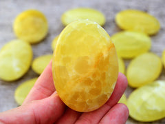 One lemon yellow calcite palm stone 45mm on hand with background with some crystals on wood table