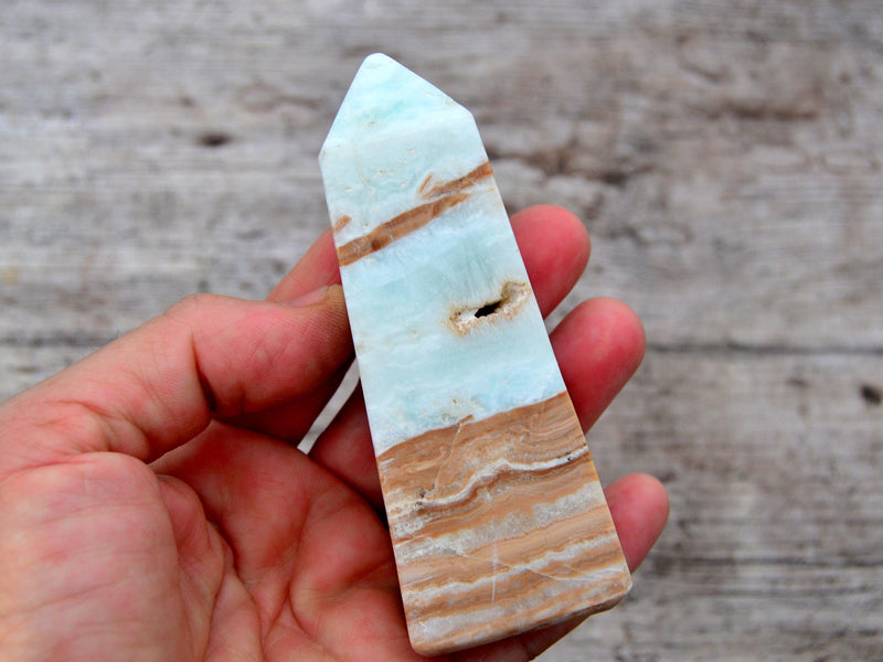 One caribbean blue calcite crystal tower 90mm on hand with wood background 