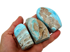 Three blue aragonite free form crystals 60mm on hand with white background