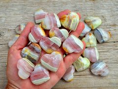 Ten pink banded onyx heart crystals 30mm on hand with background with some hearts on wood table