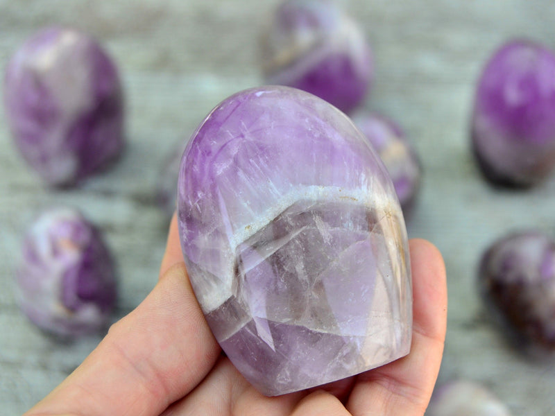One amethyst free form 55mm on hand with background with some crystals on wood table