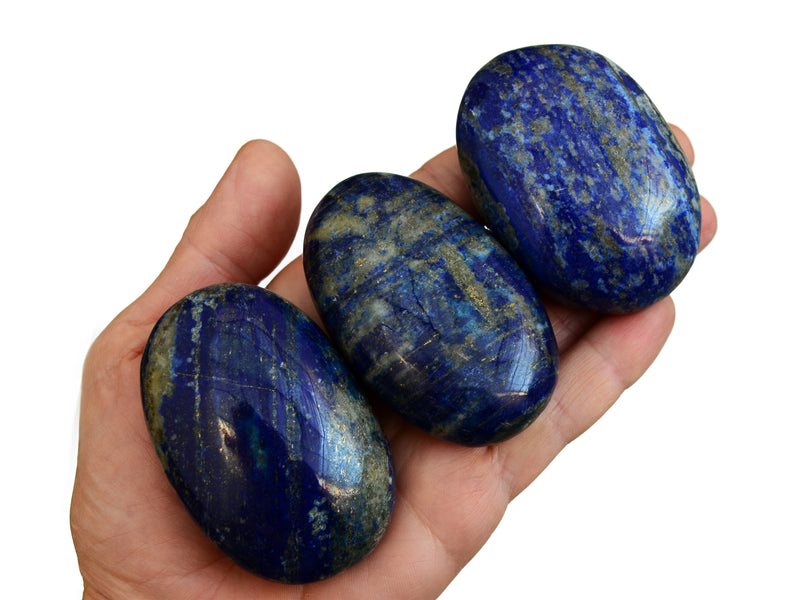 Three lapis lazuli palm stone crystals 70mm on hand with white backround