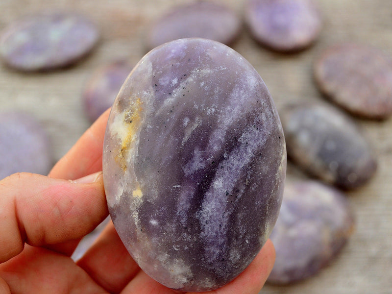 Lepidolite palm stone 80mm on hand with background with several crystals on wood table