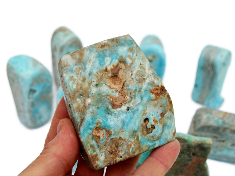 One blue aragonite free form crystal 70mm on hand with background with some stones on white