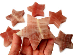 One rose calcite star crystal 80mm on hand with background with some stars on white