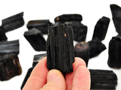 One raw black tourmaline cathedral stone 40mm on hand with background with some crystals on white