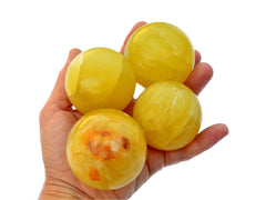 Four lemon calcite sphere crystals 50mm-65mm on hand with white background