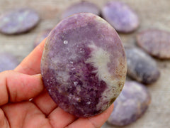 Lepidolite palm stone 75mm on hand with background with several crystals on wood table