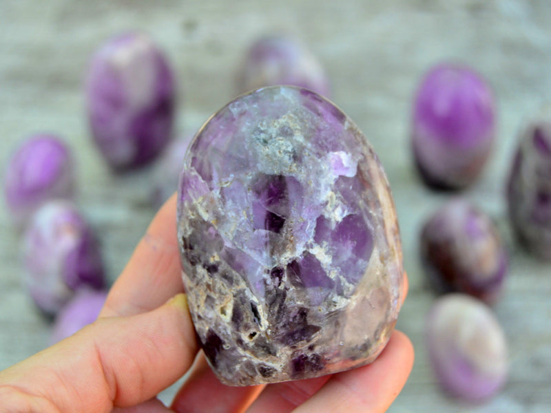 One amethyst free form 70mm on hand with background with some crystals on wood table