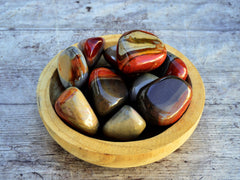 Several large desert jasper tumbled stones inside a wood bowl on wood table