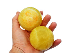 Two lemon calcite sphere stones 65mm on hand with white background