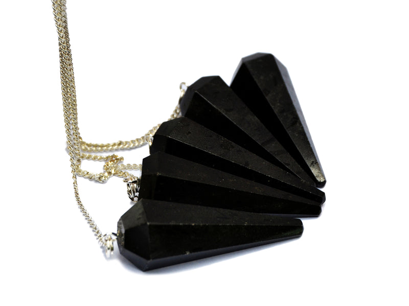 Five black tourmaline hexagonal point pendulums with silver chain holding on white background