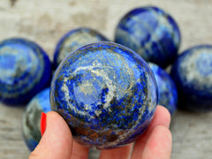 One blue lapis lazuli sphere crystal 55mm on hand with background with some balls on wood table