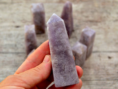 One lepidolite tower 90mm on hand with background with some obelisks on wood table