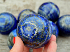 One blue lapis lazuli sphere crystal 55mm on hand with background with some balls on wood table