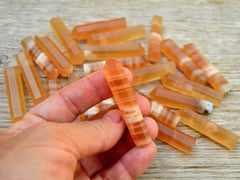 One honey calcite crystal point 55mm onhand with background with several crystals on wood table