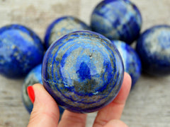 One blue lapis lazuli sphere crystal 50mm on hand with background with some lapis balls on wood table